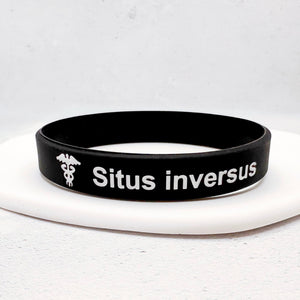 A black silicone wristband with white text reading 'Situs inversus' and a white caduceus symbol