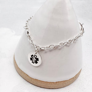 sterling silver chain bracelet with a round tag featuring the star of life medical symbol on a white surface