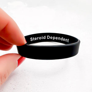 Black wristband with 'Steroid Dependent' text held by a hand on a white background