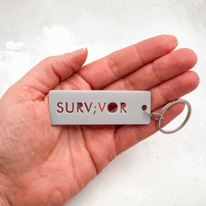 Survivor semicolon acrylic keychain shown held in hand for scale