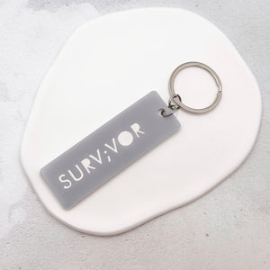 Minimalist grey acrylic Survivor semicolon keychain on neutral background