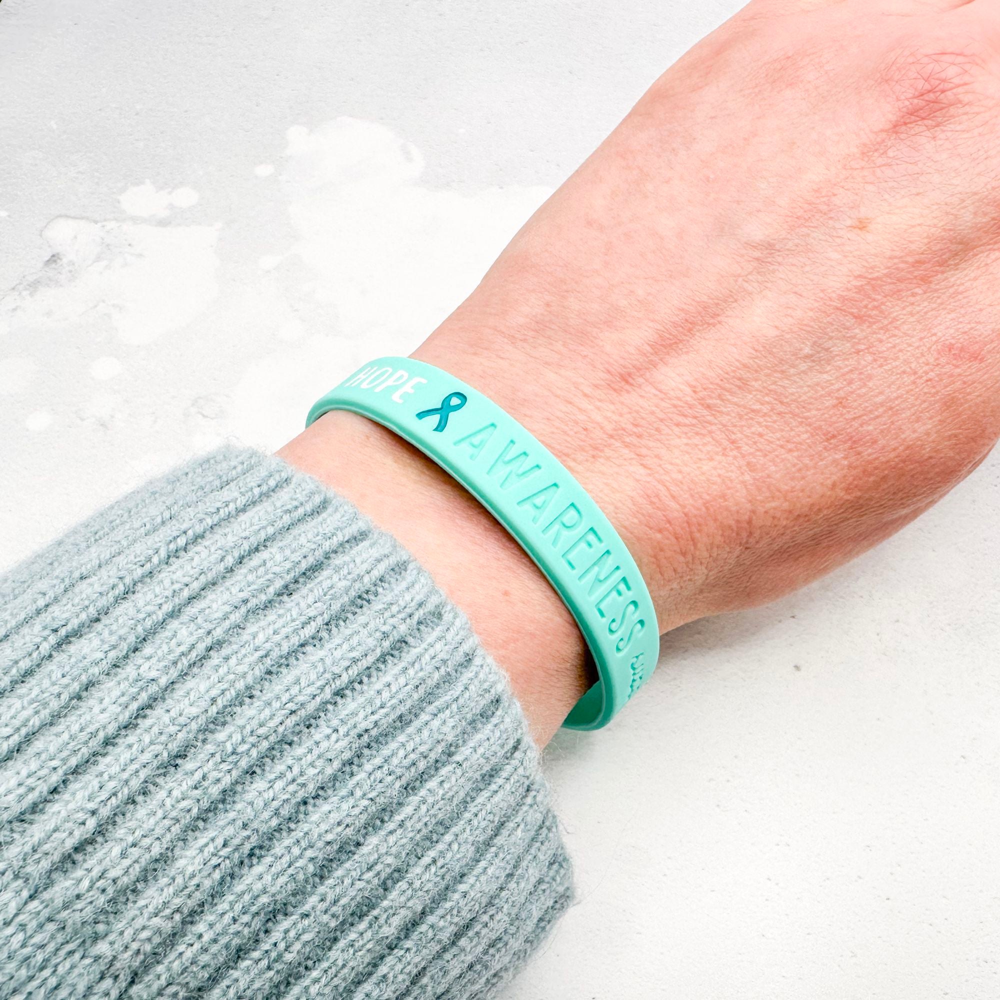 teal silicone wristband engraved with ‘Hope & Awareness’ worn on person's wrist