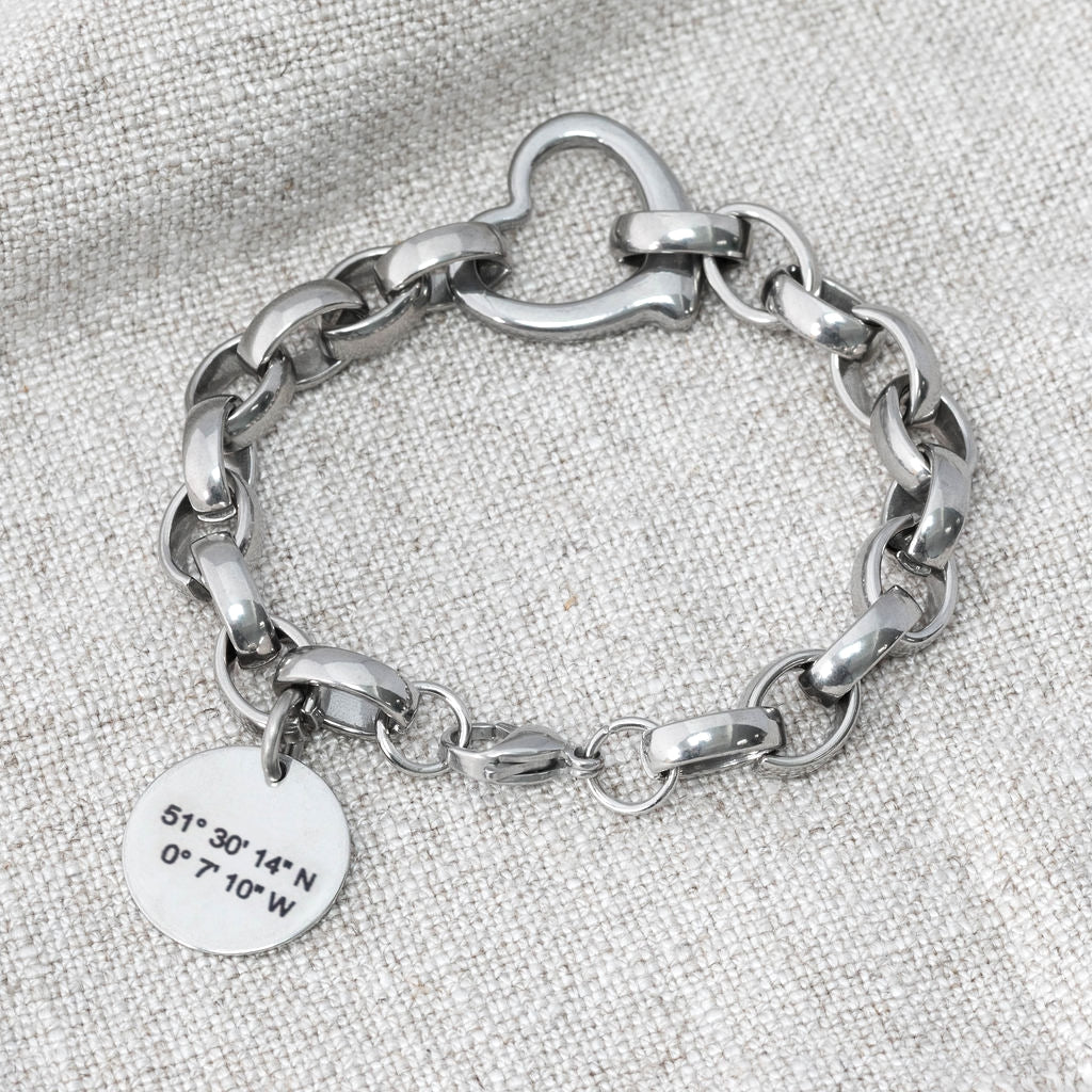 Chunky-style chain bracelet made from stainless steel with heart connector link and a round tag depicting coordinates on a grey background