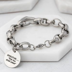 chunky-style stainless steel chain bracelet with a heart connector link and a charm tag with text on a white surface. 