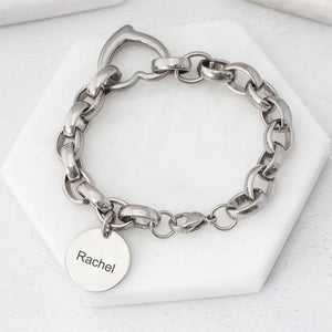 chunky-style stainless steel chain bracelet with a heart connector link and a charm tag with name on a white background. 