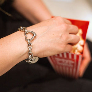 Person wearing chunky-style stainless steel chain bracelet with a heart connector link and a charm tag with name. 
