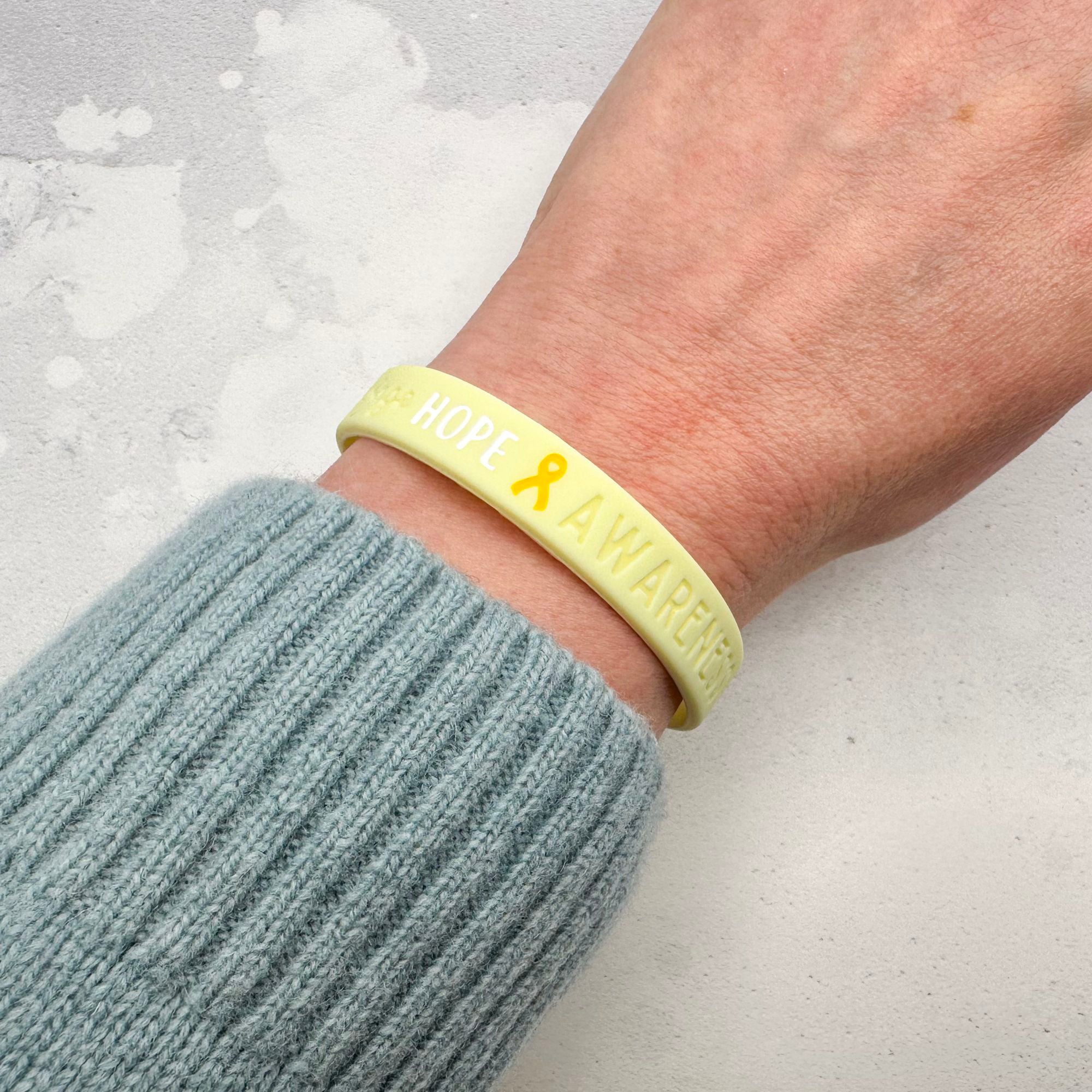 yellow silicone wristband engraved with ‘Hope & Awareness’ worn on person's wrist