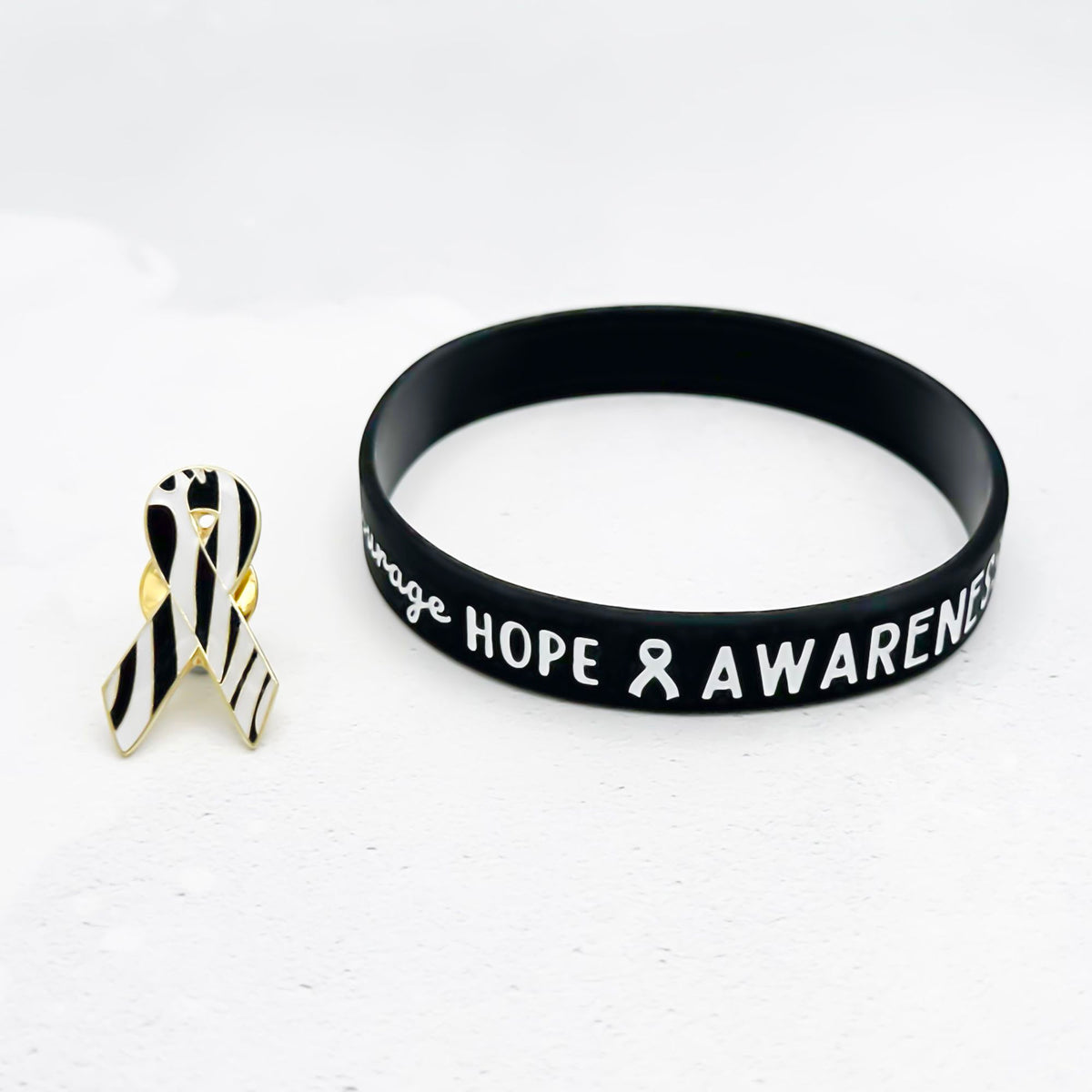 black and white silicone wristband engraved with ‘Hope & Awareness’ besides matching zebra enamel ribbon pin
